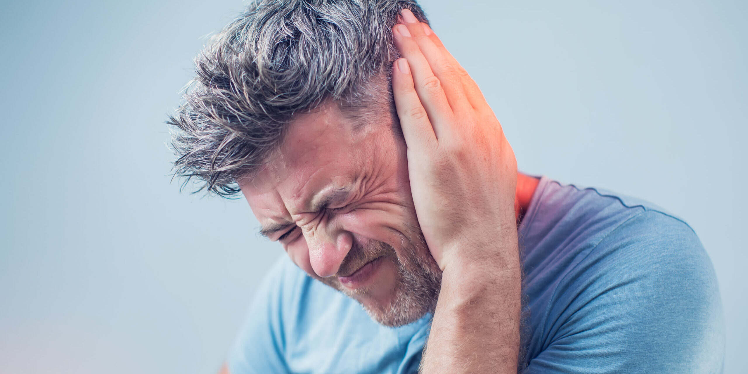 male having ear pain touching his painful head isolated on gray background