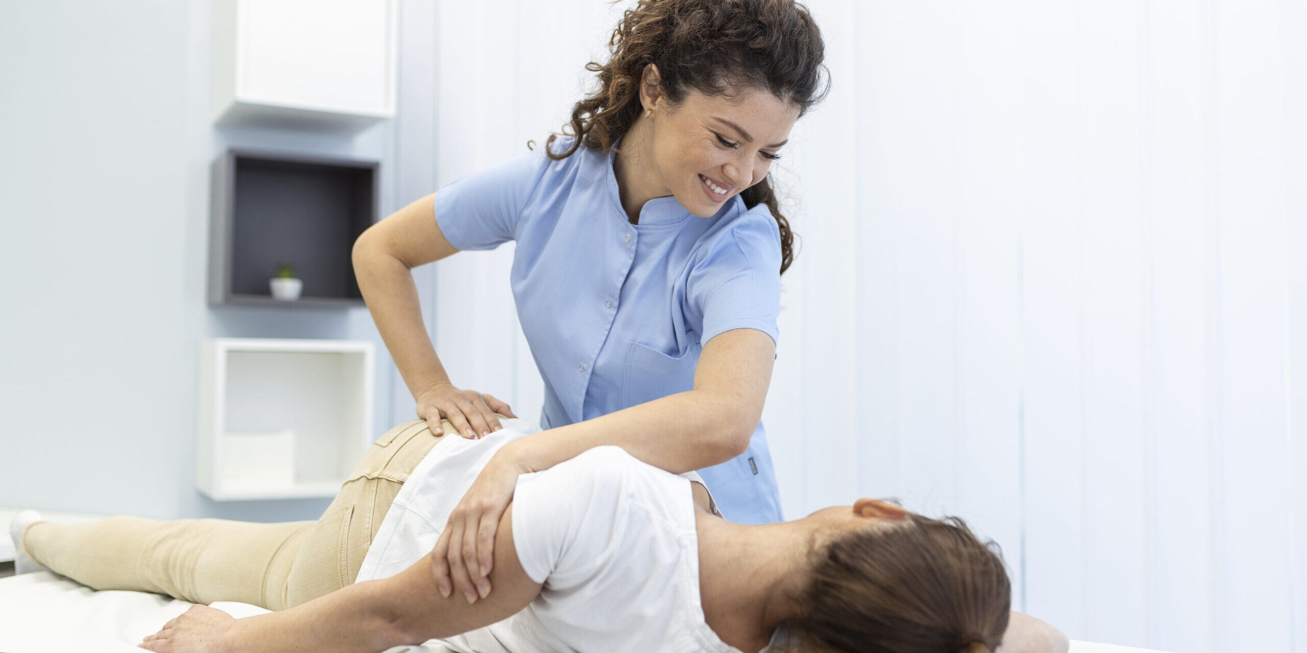 Young woman doctor chiropractor or osteopath fixing lying womans back with hands movements during visit in manual therapy clinic. Professional chiropractor during work